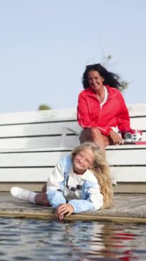 Nadir görülen bir genetik hastalıktan dolayı motor engelli sarışın küçük bir kız bir park göletinin kenarında uzanıyor, neşeli bir gülümsemeyle açık havanın tadını çıkarıyor..