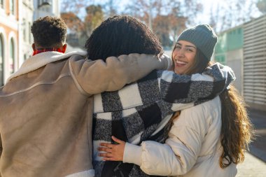 Üç genç arkadaş şehir sokaklarında yürüyor güneşli bir kış gününün tadını çıkarıyor ve birbirlerine sarılıyorlar.