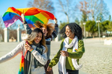 Gökkuşağı bayrağı taşıyan mutlu çoklu etnik arkadaşlar halk parkında lgbt gururunu kutluyorlar.