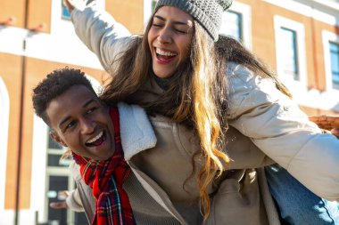 Genç adam kız arkadaşını sırtında taşıyor, hem gülüyor hem de güneşli bir kış gününün tadını çıkarıyor.