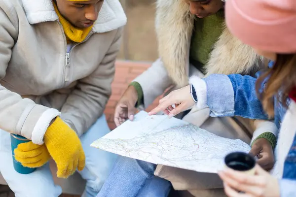 Üç turist bir harita etrafında toplandı, sıcak içecekler yudumluyor ve bir kış günü şehir gezisinde rotalarını tartışıyorlar.