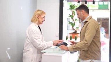 Bir adam güzellik kliniğinin resepsiyonunda duruyor, kartla ödeme yapıyor, güzellik tedavilerine odaklanmış profesyonel bir klinik ortamını vurguluyor.