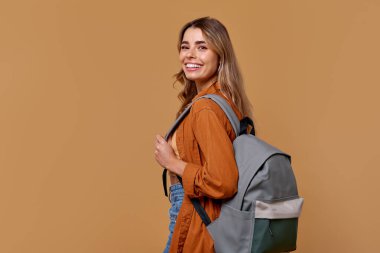Uzun saçlı, şık giyimli ve son moda sırt çantalı neşeli genç bir kadın. Mutluluk saçıyor. Bu resim, çeşitli yaratıcı projeler için cazip, seyahat ve yaşam tarzı temalarını somutlaştırır.
