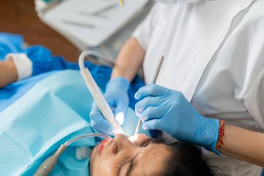 Klinikteki Hintli bir kadın müşterinin dişlerini temizlemek için matkap kullanan bir dişçi.