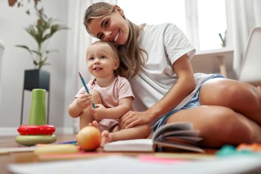 Sıcak bir evde, sevgi dolu bir anne ve yeni yürümeye başlayan bebeği renkli oyuncaklar ve sanat malzemeleri arasında yaratıcı ve bağlanmayı teşvik eden parlak, rahat bir alan yaratarak yaratıcı bir oyun oynuyorlar.