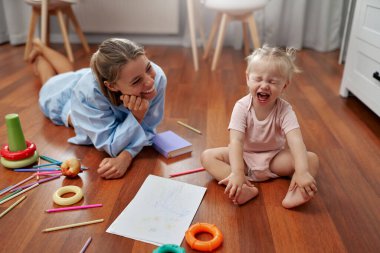 Neşeli bir anne, meraklı bebeğinin hayallerini canlandıran renkli oyuncaklarla çevrili sıcak ahşap bir zeminde canlı çizimler ve eğlenceli aktivitelerle yaratıcılığı keşfetmesini izler.