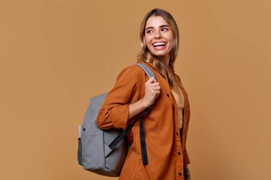 Uzun saçlı, şık giyimli ve son moda sırt çantalı neşeli genç bir kadın. Mutluluk saçıyor. Bu resim, çeşitli yaratıcı projeler için cazip, seyahat ve yaşam tarzı temalarını somutlaştırır.