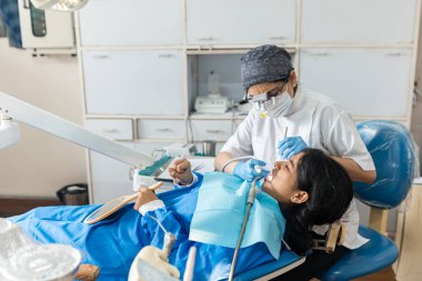 Hintli dişçi kadın özel bir klinikte dişlerini incelerken hasta şikayet ediyor.