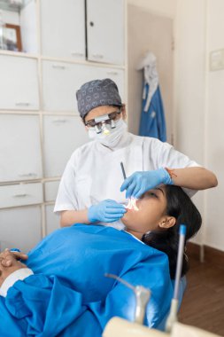 Hintli kadın doktor bir diş kliniğinde bir hastanın ağzını inceliyor.