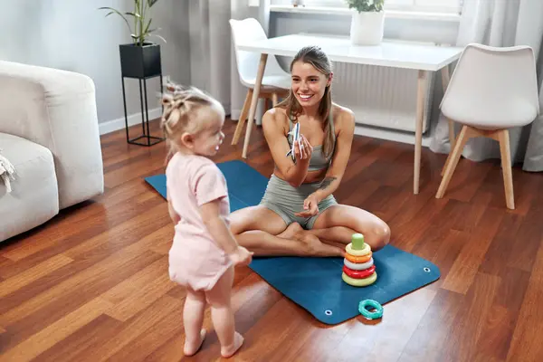 Mutlu ve neşeli bir anne evde yoga rutinini uyguluyor. Sevimli bebeği yakınlarda oynarken, harika bir uyum ve aile ortamının harika bir karışımını sergiliyor.