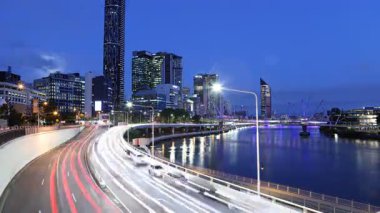 Brisbanes 'in alacakaranlıktan geceye geçişini gösteren çarpıcı bir zaman atlaması. Aydınlatılmış gökdelenler, trafikten gelen ışık yolları ve nehirdeki yansımalar dinamik bir şehir manzarası yaratıyor.