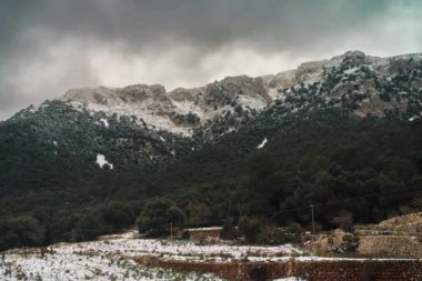 Hızlandırılmış büyüleyici bir zaman atlaması, engebeli tepelerin üzerinde bulutlar sürüklenirken karla kaplı Mallorcas dağlarını yakalıyor. Kış manzarası aşağıdaki yemyeşil ormanla çok güzel tezat oluşturuyor..