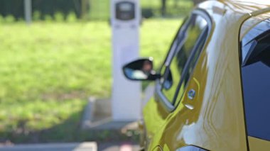 Açık hava şarj istasyonunda çalışan sarı elektrikli bir araba modern sürdürülebilir ulaşım çözümleri sergiliyor..