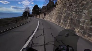 Kışın İsviçre, Lavaux 'da çarpıcı bir sahil yolu. Motosikletlinin perspektifinden çekilen Geneva Gölü ve çevresindeki dağların çarpıcı manzarasını gösteriyor..