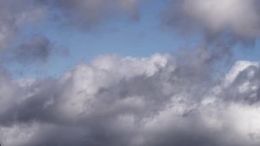 Tüylü gri bulutların güzel bir zaman dilimi canlı mavi gökyüzünde hızla hareket ediyor. Işık ve gölgenin karışımı dinamik ve barışçıl bir gökyüzü yaratır, hava değişimlerini gösterir..