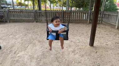 Kıvırcık saçlı, mavi şortlu, salıncakta sallanan tahta çitlerle ve ağaçlarla çevrili bir çocuk..