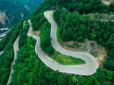 Yazın dağ kıvrımlı yolu ve yeşil ormanın havadan görünüşü. Dolomitler, İtalya. Dağ geçidindeki virajlı yol manzarası, baharda ağaçlar. Ormandan geçen yol. Karamsar, yol manzaralı