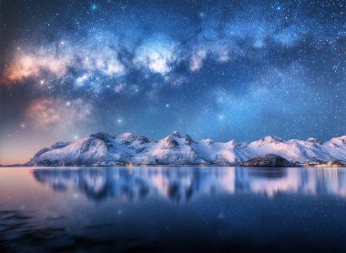 Samanyolu kış gecelerinde karlı dağların ve fiyortların üzerinde. Karlı kayalarla panoramik manzara, mavi yıldızlı gökyüzü, suda yansıma. Lofoten Adaları, Norveç. Boşluk. Denizin üzerinde parlayan Samanyolu