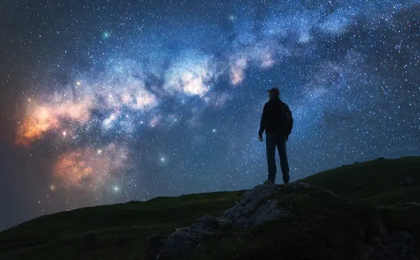 Parlayan Samanyolu ve yıldızlı gecede dağın zirvesinde bir adam. Tepede parlak yıldızlı bir adamın silueti. Galaksi. Samanyolu ile uzay manzarası. Gece manzarası. Seyahat geçmişi. Kavram