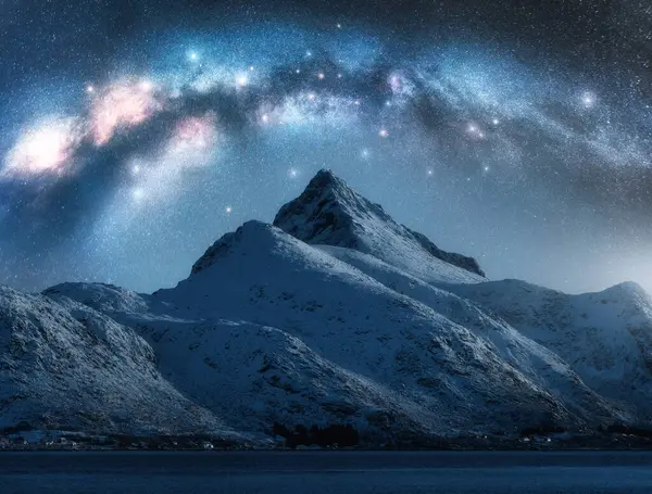 Samanyolu kışın yıldızlı gecesinde güzel karlı dağın üzerinde. Lofoten Adaları, Norveç. Parlayan Samanyolu kemeri, yıldızlar, karlı kayalar ve fiyortlu gökyüzü ile renkli bir manzara. Boşluk. Doğa
