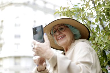 Dışarıda elinde cep telefonu olan yaşlı bir kadın.