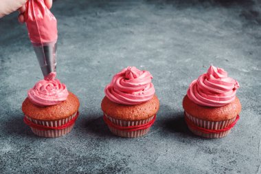 Yukarıdan gelen pasta çantasıyla isimsiz aşçı pembe kremalı şenlikli kapkekleri süslüyor.