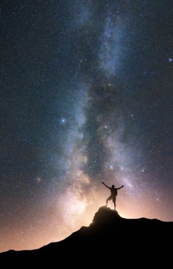Samanyolu ve kollarını kaldırmış mutlu bir adam yıldızlı gecede dağın zirvesinde. Adamın silueti, tepe, gökyüzü yazın parlayan yıldızlar. Galaksi. Uzay arkaplanı. Samanyolu ile dikey manzara