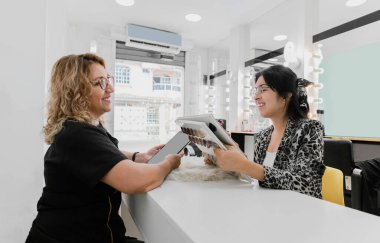 İki İspanyol kadın bir kuaförde saç örnekleri kataloğuna bakıyorlar.