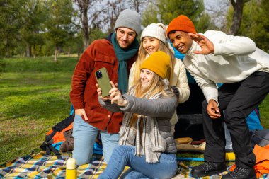 Birlikte kamp yapmaktan keyif alan dört mutlu arkadaş doğayla çevrili güzel bir parkta selfie çekiyorlar.