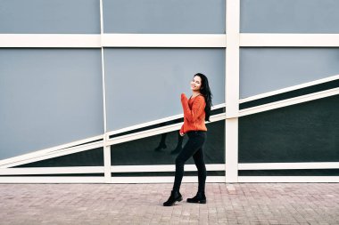 Rüzgârlı bir günde modern binanın yanında gülümseyen ve dikilen günlük kıyafetli neşeli etnik kadın vücudu.