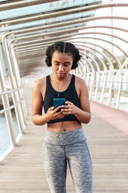 Spor giyim sektöründe genç bir bayan sporcu antrenmandan sonra dinlenirken cep telefonuyla gülümsüyor ve konuşuyor.