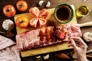 Masada çeşitli malzemelerle yemek pişirirken çiğ domuz pirzolası üzerine barbekü sosu döken isimsiz bir aşçının tepesinden.