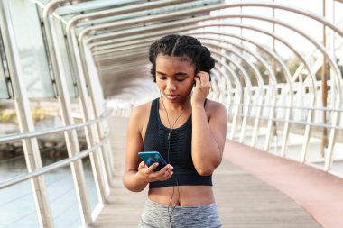 Spor giyim sektöründe genç bir bayan sporcu antrenmandan sonra dinlenirken cep telefonuyla gülümsüyor ve konuşuyor.