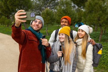 Bir grup genç yürüyüşçü, ormanda yürüyüş yaparken akıllı telefonlarıyla selfie çekiyor.