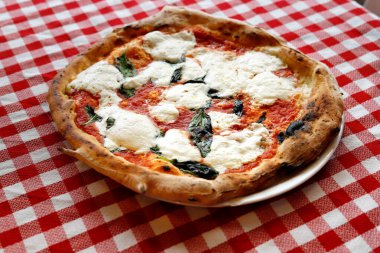 Damalı masa örtüsü üzerinde margherita pizza, yakın çekim.