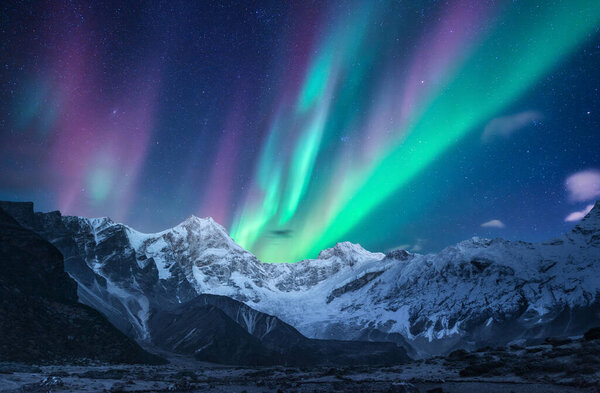 Северное сияние над снежными горами ночью в Лофотене, Норвегия. Aurora borealis над покрытыми снегом скалами. Зимний пейзаж с полярными огнями, горная вершина. Прекрасное звездное небо с сиянием