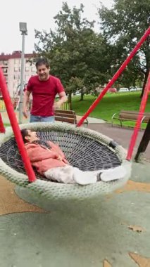 Sevgi dolu bir baba, halk parkında salıncakta sallanan beyin felci geçiren oğluna bakar. Görüntü, açık havada bir bakım ve destek anı yakalıyor..