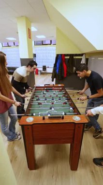 Bir grup arkadaş, zihinsel sağlık merkezinde, bakıcıları, rahatlamaları, sosyal etkileşimleri ve refahı modern tesislerle destekleyici bir ortamda vurgulayan masa futbolu oynuyorlar..