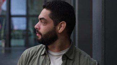 Sıradan giyinmiş bir Latin adam şehir ortamında duruyor, çağdaş bir mekanda tefekkür, güven ve modern erkeksiliği aktarıyor..