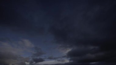 Karanlık bir ufuk üzerinde ışıktan kara bulutlara geçişi gösteren, hızla değişen bulut kalıplarını yakalayan bir zaman kaydıdır..