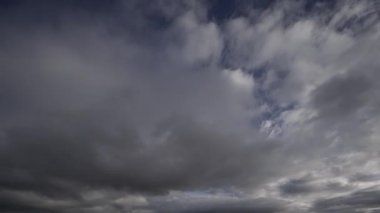Fırtınalı bulutların karanlık gökyüzünde hızlı bir şekilde hareket edişini gösteren ve parlak bir şekilde gün ışığından griye kayan bir video..