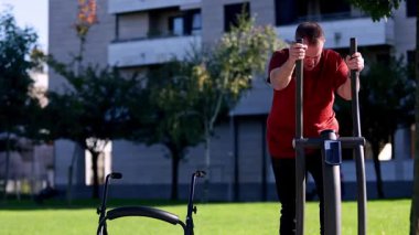 Zihinsel engelli bir yetişkin, halka açık bir parkta eliptik bir makine kullanır, sağlığını, gücünü ve bağımsızlığını geliştirmek için fiziksel aktiviteler yapar.