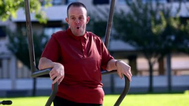 Zihinsel engelli yetişkin bir adam, sağlıklı ve kapsayıcı rutininin bir parçası olarak parktaki bir spor salonunda fiziksel aktivitenin ve temiz havanın tadını çıkarır.