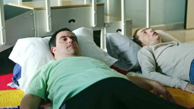 Zihinsel engelli iki yetişkin, kapalı bir alanda yastıklı minderlere uzanıp, sükunet, rahatlık ve duygusal refahı sağlama amaçlı bir gevşeme oturumuna katılıyorlar.