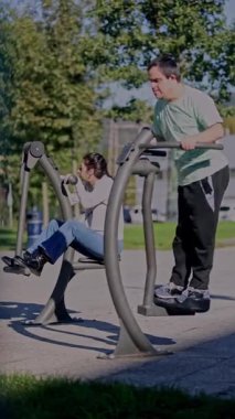 Zihinsel engelli bir erkek ve kadın, açık hava fitness ekipmanlarını kullanır, fiziksel aktiviteyi, bağımsızlığı ve şehir ortamında sağlıklı rutinleri teşvik eder.