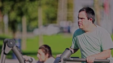 Zihinsel engelli yetişkin bir adam, sağlık ve kişisel özerkliğini desteklemek için fiziksel aktivite yapan, odaklanmış ve kararlı bir şekilde açık hava fitness ekipmanı kullanır.