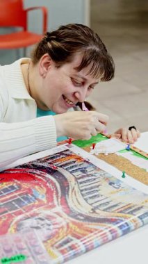 Zihinsel engelli bir kadın dikkatle elmas resim tahtasına boncuk yerleştirir. Bir sanat ve zanaat seansında odaklanma ve azim gösterir.