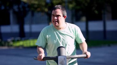 Açık hava spor aletleri üzerine zihinsel engelli bir adam halka açık bir parkta fiziksel sağlığı, bağımsızlığı ve topluma aktif katılımı teşvik ediyor..