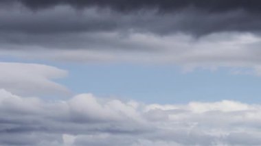 Bu zaman ayarlı video, gökyüzünde hızla ilerleyen koyu ve kabarık beyaz bulutların dinamik hareketlerini yakalar, dramatik ve sürekli değişen bir hava sahnesi sunar..
