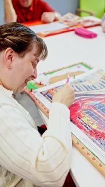 Zihinsel engelli bir kadın dikkatle elmas resim tahtasına boncuk yerleştirir. Bir sanat ve zanaat seansında odaklanma ve azim gösterir.